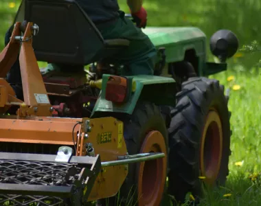 Micro-tracteur agricole attelé à un gyrobroyeur, utilisé pour débroussailler de l’herbe haute dans un espace vert.